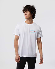 Amidst a simple backdrop, an individual with curly hair wears the Psycho Bunny MENS CHICAGO CITY TEE - B6U551W1PC, made from soft Pima cotton. The tee sports a subtle chest graphic of red stars, and they stand calmly with arms relaxed.