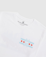 The Psycho Bunny MENS CHICAGO CITY TEE - B6U551W1PC is a white Pima cotton tee showcasing light blue and red flag-like stars. Featuring the classic logo and distinct branding inside the neckline, it blends comfort with style effortlessly.
