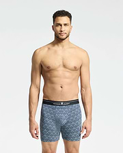 A man with short curly hair stands against a plain white background, wearing Psycho Bunny's Mens 2 Pack Boxer Briefs (B6V481F200) featuring a black waistband. He looks directly at the camera, showcasing the comfort and style of the breathable stretch Pima cotton.