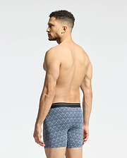 A man stands with his back turned, wearing Psycho Bunny's MENS 2 PACK BOXER BRIEF - B6V481F200 crafted from stretch Pima cotton in a blue pattern against a plain light gray background.
