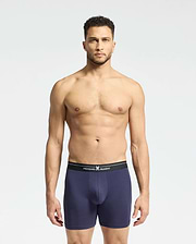 A man with short dark hair and a neutral expression models the Psycho Bunny MENS 2 PACK BOXER BRIEF - B6V481F200 against a plain background, showcasing navy blue Pima cotton with a black waistband featuring white text.