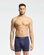 A man with short dark hair and a neutral expression models the Psycho Bunny MENS 2 PACK BOXER BRIEF - B6V481F200 against a plain background, showcasing navy blue Pima cotton with a black waistband featuring white text.