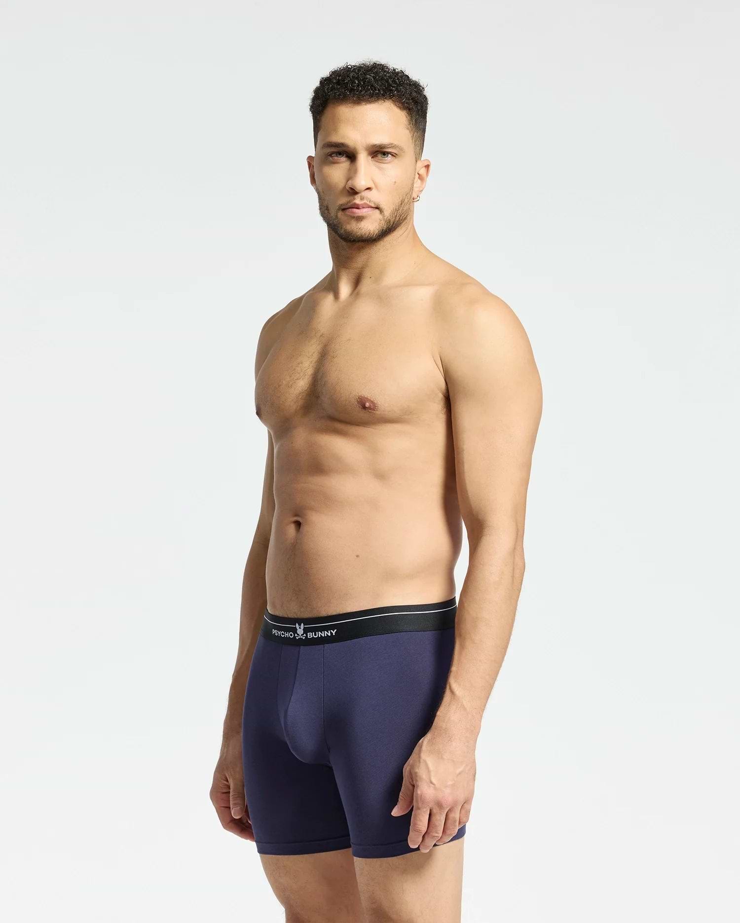 A man faces forward in navy MENS 2 PACK BOXER BRIEF - B6V481F200 by Psycho Bunny, crafted from soft Pima cotton with a black waistband, showcasing the comfortable stretch fit against a plain backdrop.