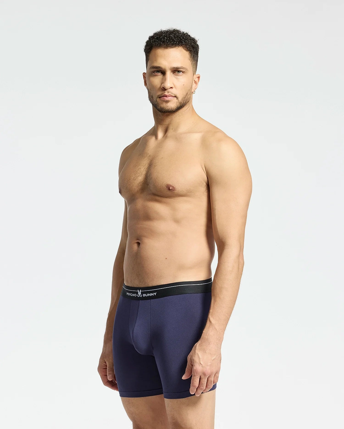 A man faces forward in navy MENS 2 PACK BOXER BRIEF - B6V481F200 by Psycho Bunny, crafted from soft Pima cotton with a black waistband, showcasing the comfortable stretch fit against a plain backdrop.