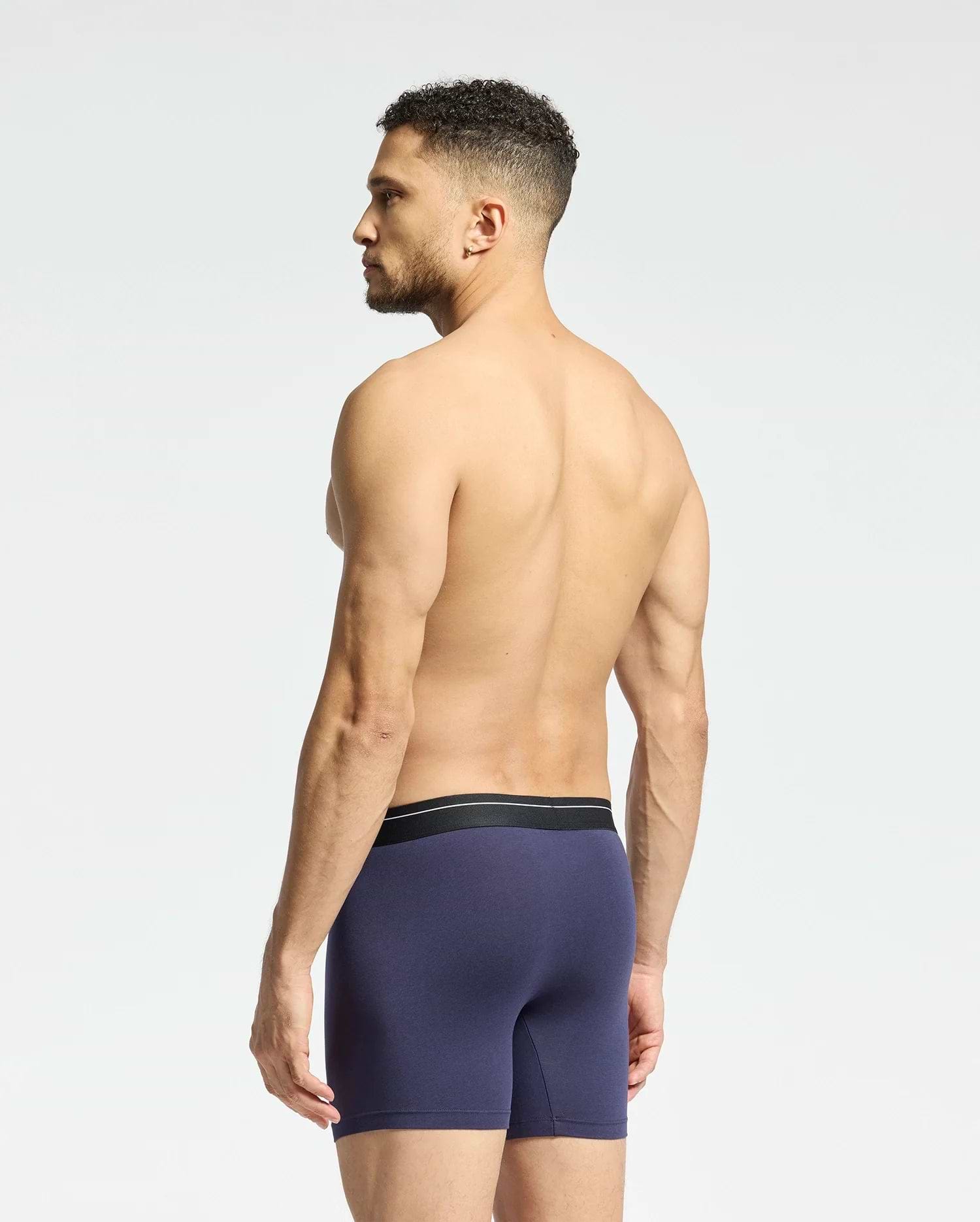 A shirtless man with short dark hair stands slightly to the side in Psycho Bunny's MENS 2 PACK BOXER BRIEF - B6V481F200. The briefs are dark blue with a black waistband and made of soft Pima cotton, set against a plain light background.