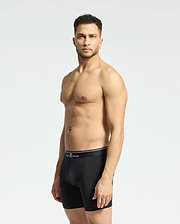 A man with short curly hair stands against a plain light backdrop, wearing Psycho Bunny MENS SOLID KNIT 2 PACK BOXER BRIEF - B6V906ARCM in black. He faces slightly to the side with a neutral expression.