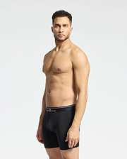 A man with short curly hair stands against a plain light backdrop, wearing Psycho Bunny MENS SOLID KNIT 2 PACK BOXER BRIEF - B6V906ARCM in black. He faces slightly to the side with a neutral expression.