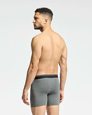 A shirtless man with short curly hair faces away, displaying Psycho Bunny's MENS SOLID KNIT 2 PACK BOXER BRIEF - B6V906ARCM in gray. These comfy Pima cotton boxers feature a sleek black waistband. He stands against a plain white background.