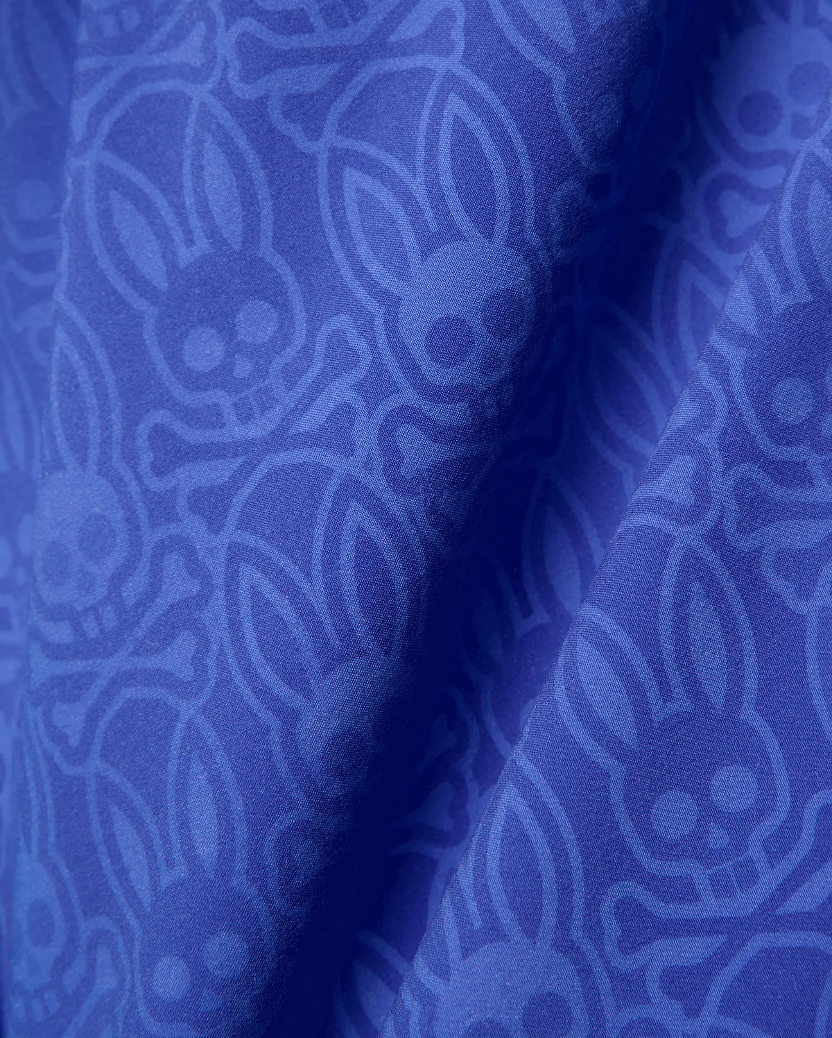 Mens Samos Hydrochromic Printed Swim Trunk in royal blue, featuring a subtle tonal all-over Psycho Bunny skull and crossbones logo pattern on smooth fabric.