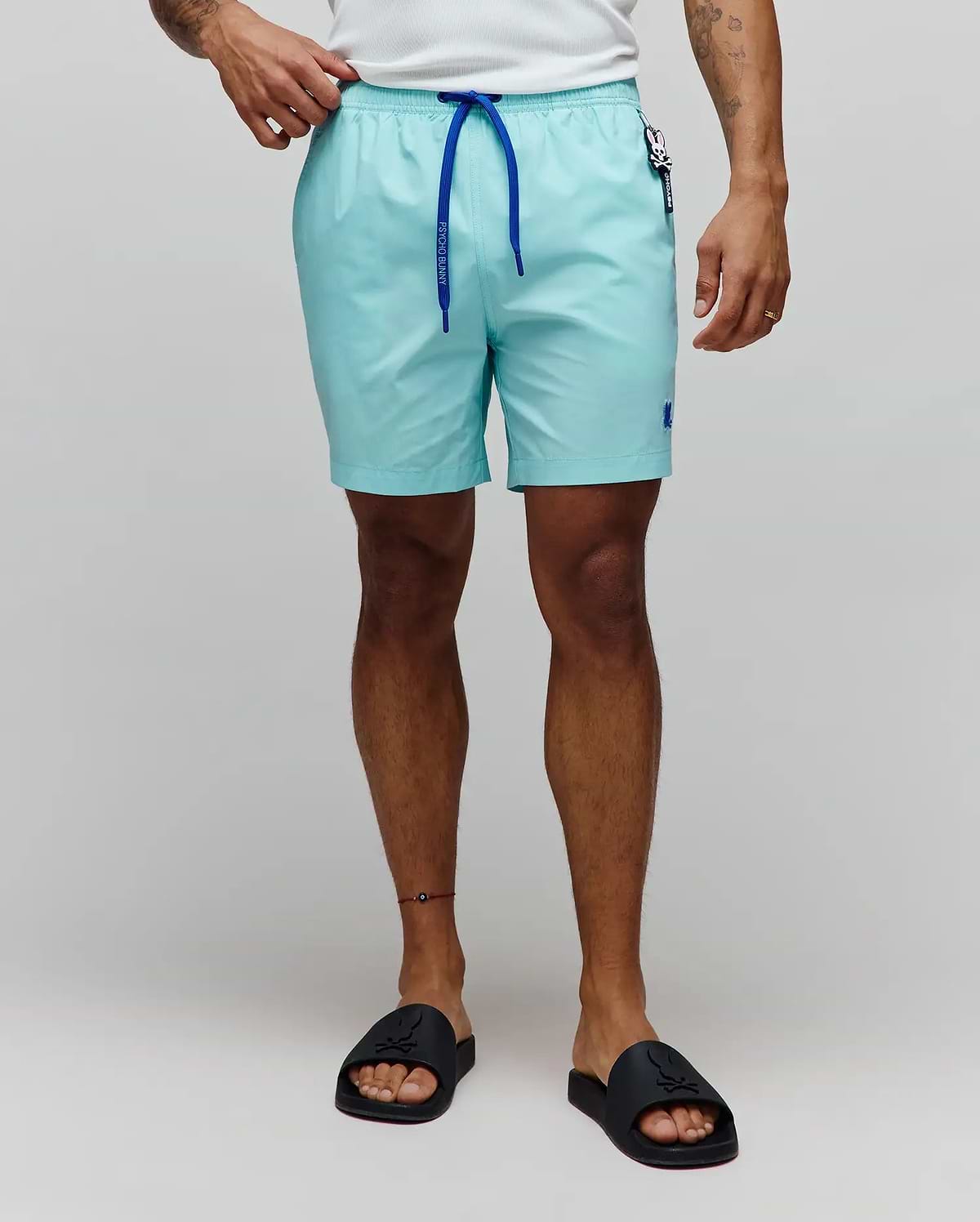 Mens Samos Hydrochromic Printed Swim Trunk in aqua, featuring a smooth texture, royal blue drawstring with Psycho Bunny text, small embroidered blue bunny skull logo on the left leg, and a branded tag on the right hip.