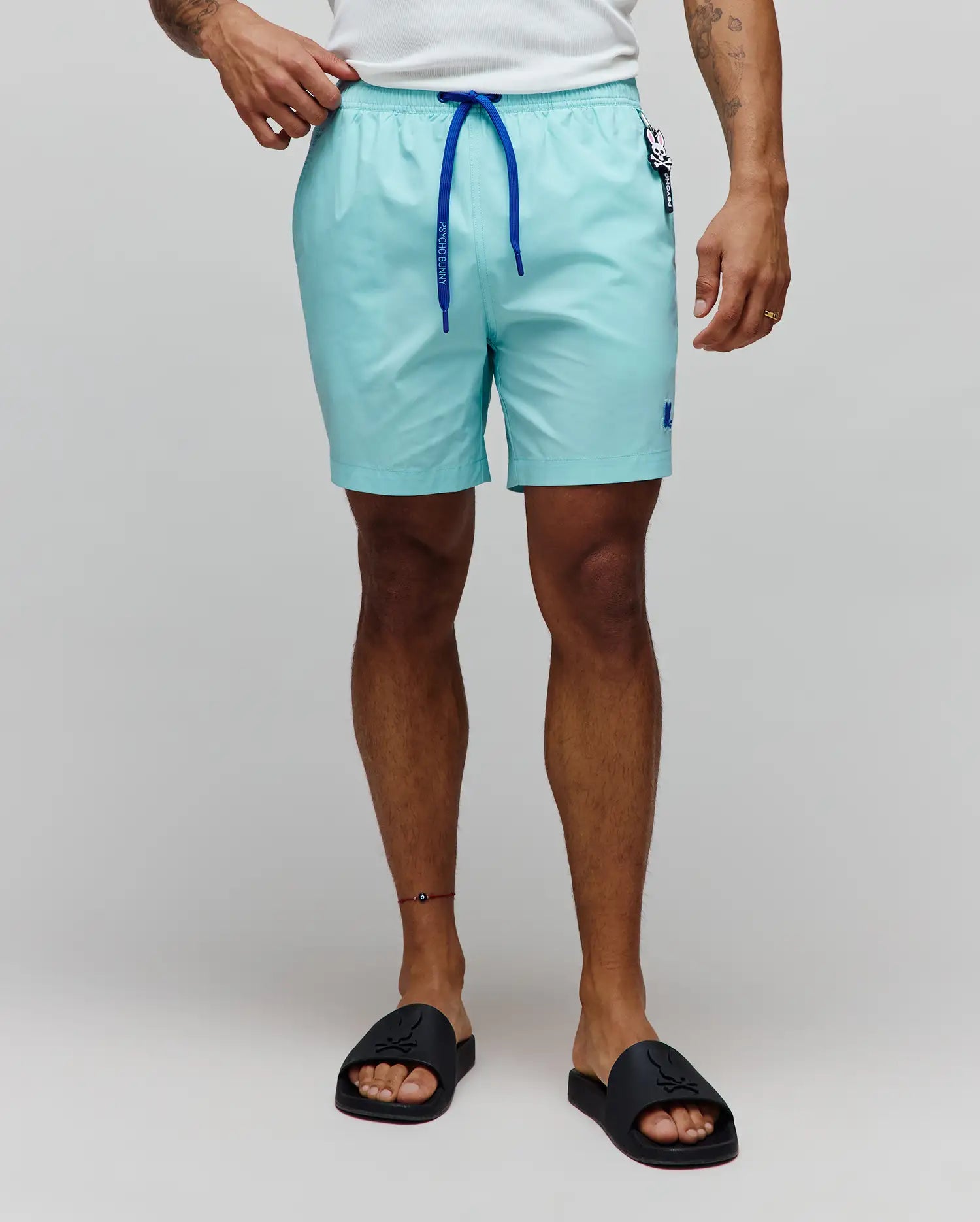 Mens Samos Hydrochromic Printed Swim Trunk in aqua, featuring a smooth texture, royal blue drawstring with Psycho Bunny text, small embroidered blue bunny skull logo on the left leg, and a branded tag on the right hip.