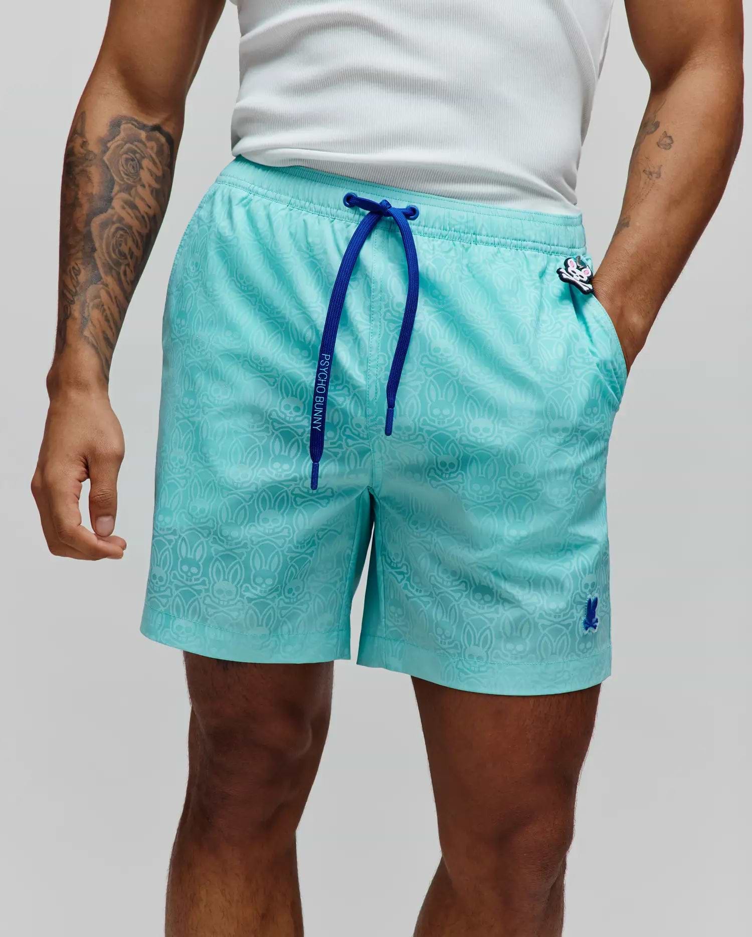 Mens Samos Hydrochromic Printed Swim Trunk in aqua, with a subtle all-over bunny skull pattern, royal blue drawstring featuring Psycho Bunny text, and an embroidered bunny skull logo on the left leg.
