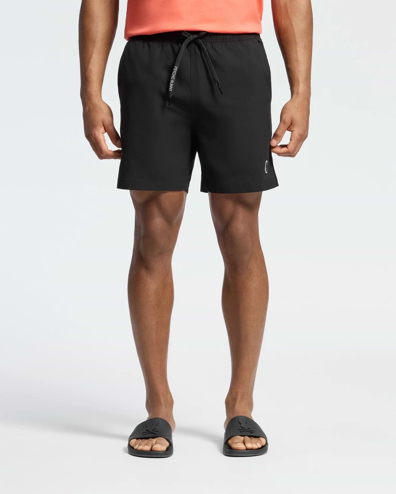 Mens Samos Hydrochromic Printed Swim Trunk in black, featuring a classic fit, smooth quick-dry fabric, a drawstring with white Psycho Bunny text, and a subtle white bunny skull logo on the lower left leg.