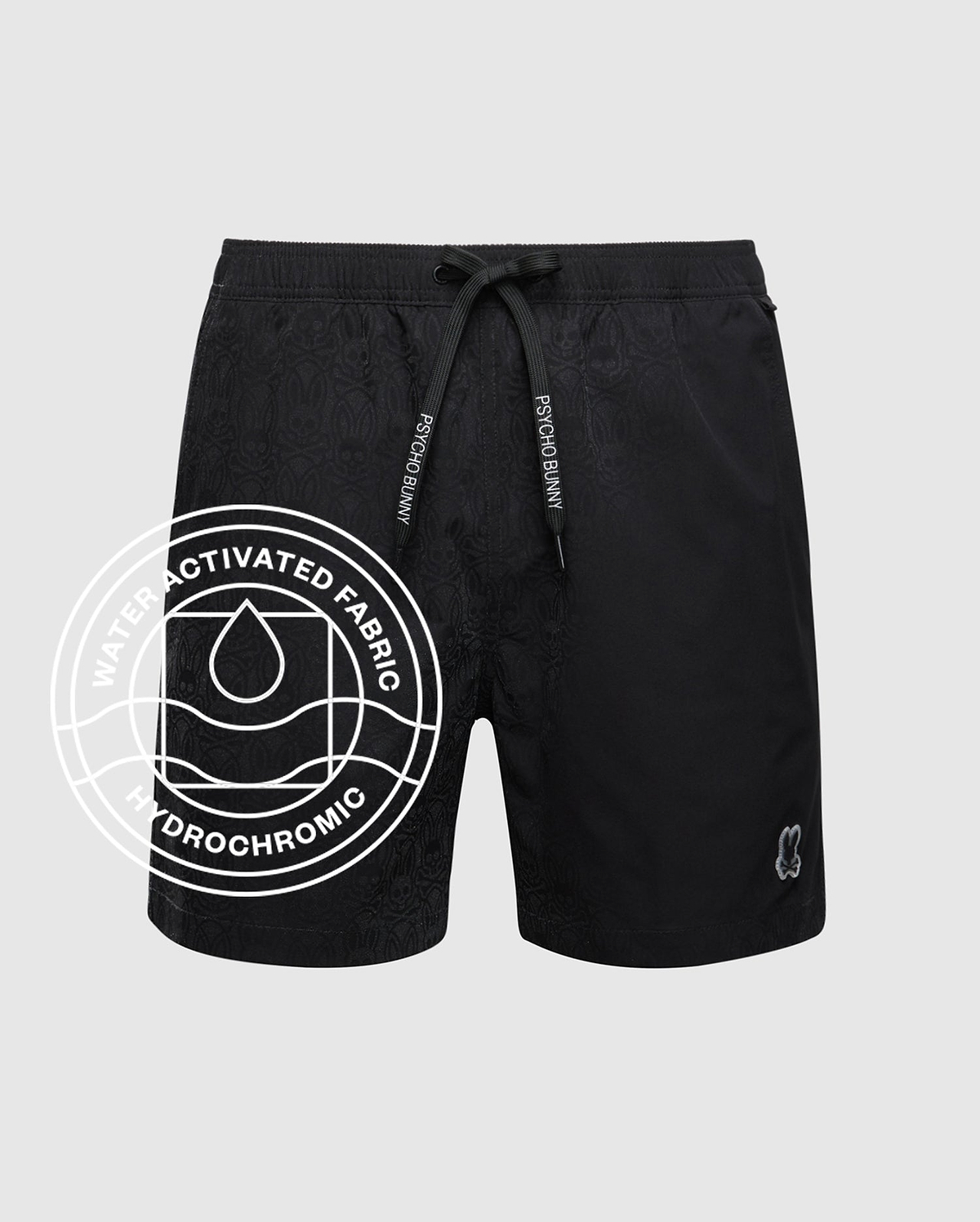 Mens Samos Hydrochromic Printed Swim Trunk, a black swim trunk with a subtle all-over hydrochromic bunny skull pattern, white Psycho Bunny drawstring text, and a small embroidered bunny skull logo on the left leg.