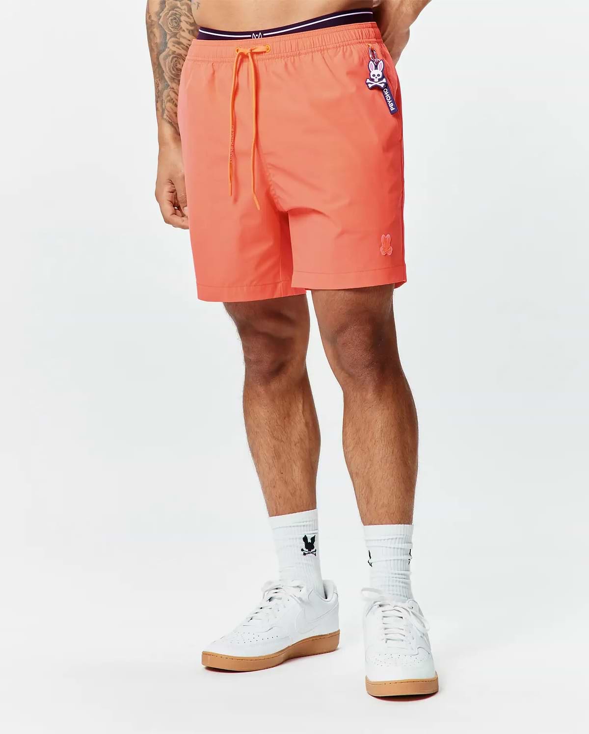 Mens Samos Hydrochromic Printed Swim Trunk in vibrant coral, relaxed fit, smooth fabric, orange drawstring, purple waistband, small embroidered bunny skull, and Psycho Bunny logo tag.