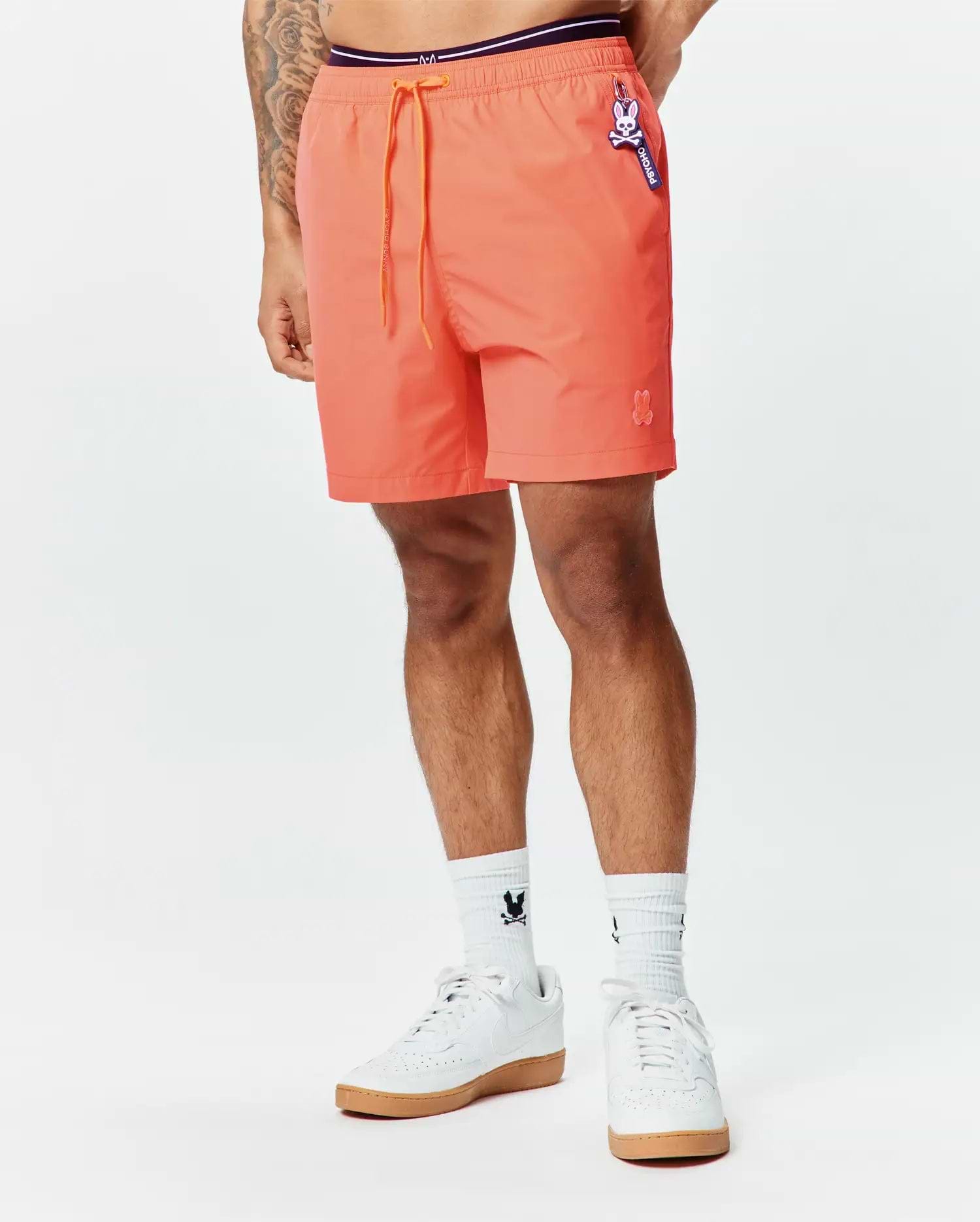 Mens Samos Hydrochromic Printed Swim Trunk in vibrant coral, relaxed fit, smooth fabric, orange drawstring, purple waistband, small embroidered bunny skull, and Psycho Bunny logo tag.