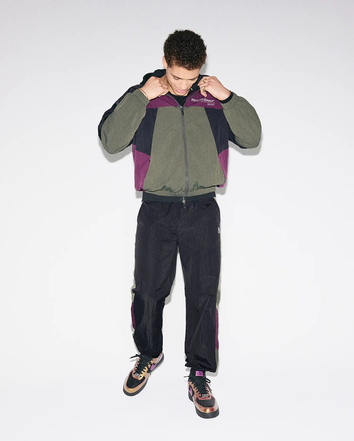 Olive, black, and purple colorblock crinkled nylon windbreaker jacket with Psycho Bunny chest text logo, paired with matching Mens Alder Nylon Colorblock Pant featuring side stripes and an embroidered bunny skull.