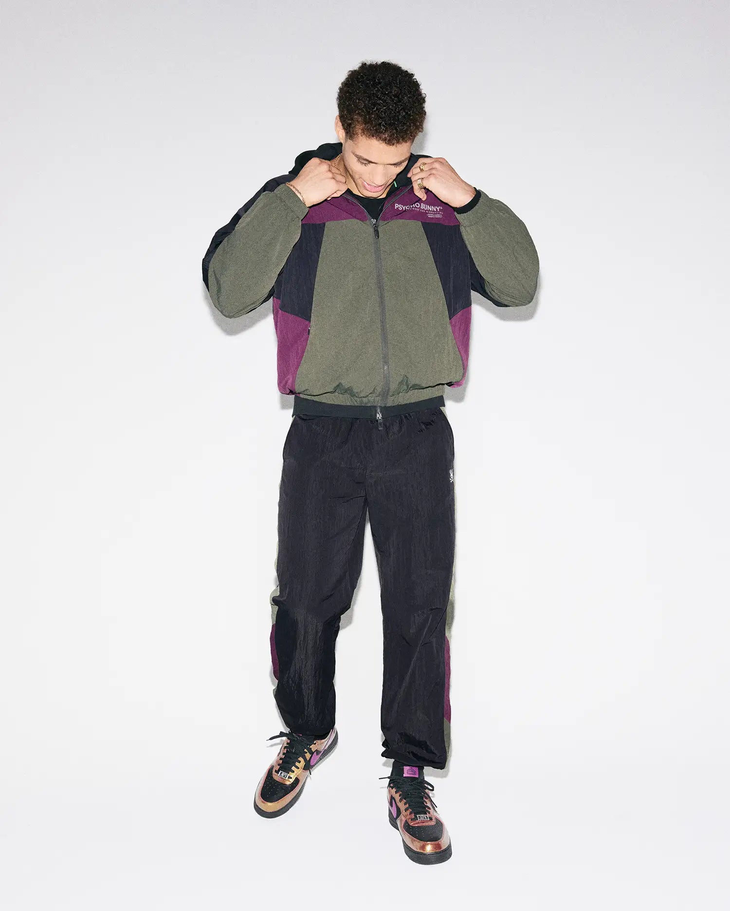 Olive, black, and purple colorblock crinkled nylon windbreaker jacket with Psycho Bunny chest text logo, paired with matching Mens Alder Nylon Colorblock Pant featuring side stripes and an embroidered bunny skull.