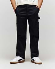 A person models the Psycho Bunny KIDS RUSSELL CARPENTER PANT (KB0600001) with cargo pockets and white sneakers, standing with hands in pockets against a plain light background.