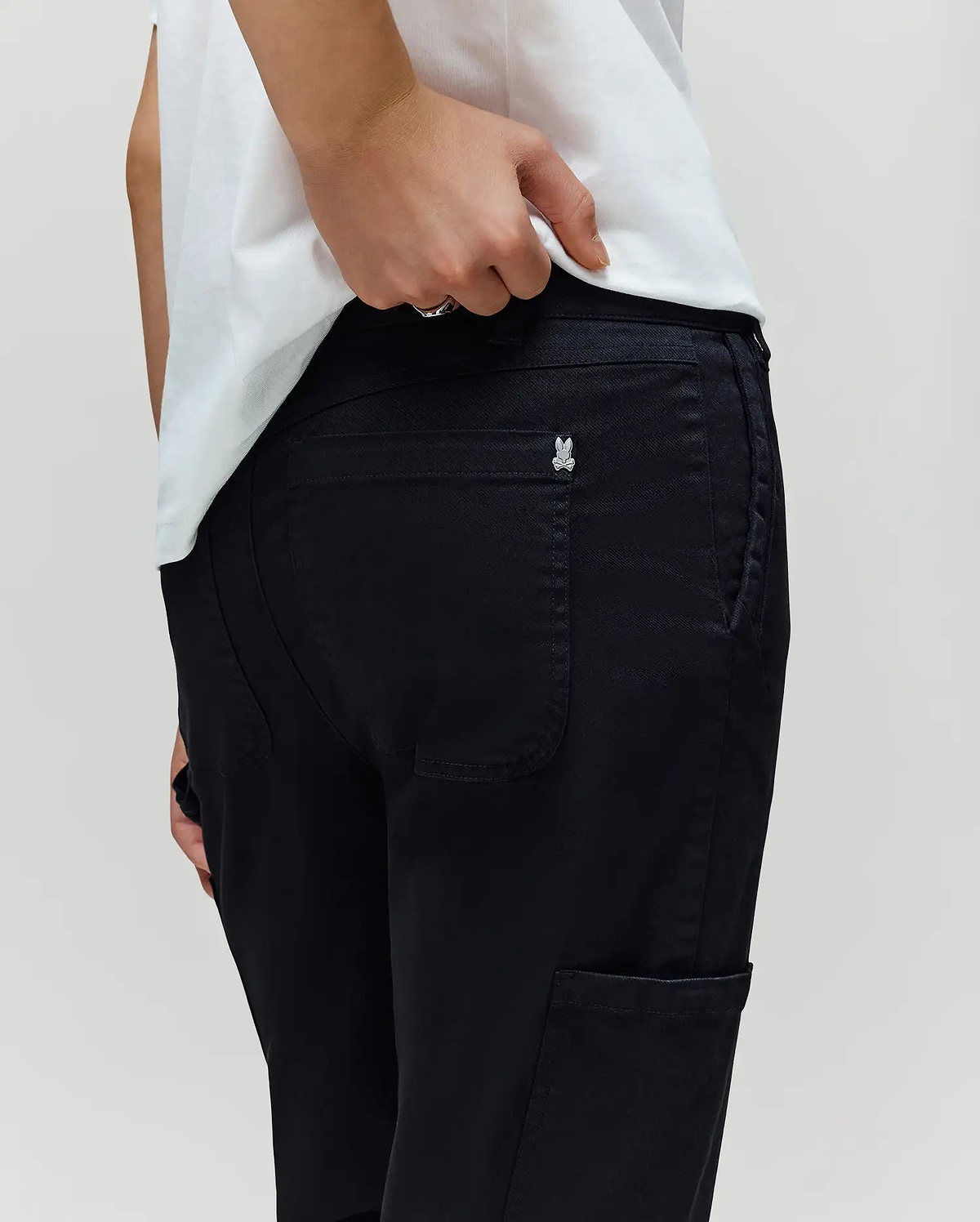 A person in a white shirt and black Psycho Bunny KIDS RUSSELL CARPENTER PANT (KB0600001), with a silver butterfly pin on the back pocket, stands against a plain light background. The pants are styled in a regular fit.