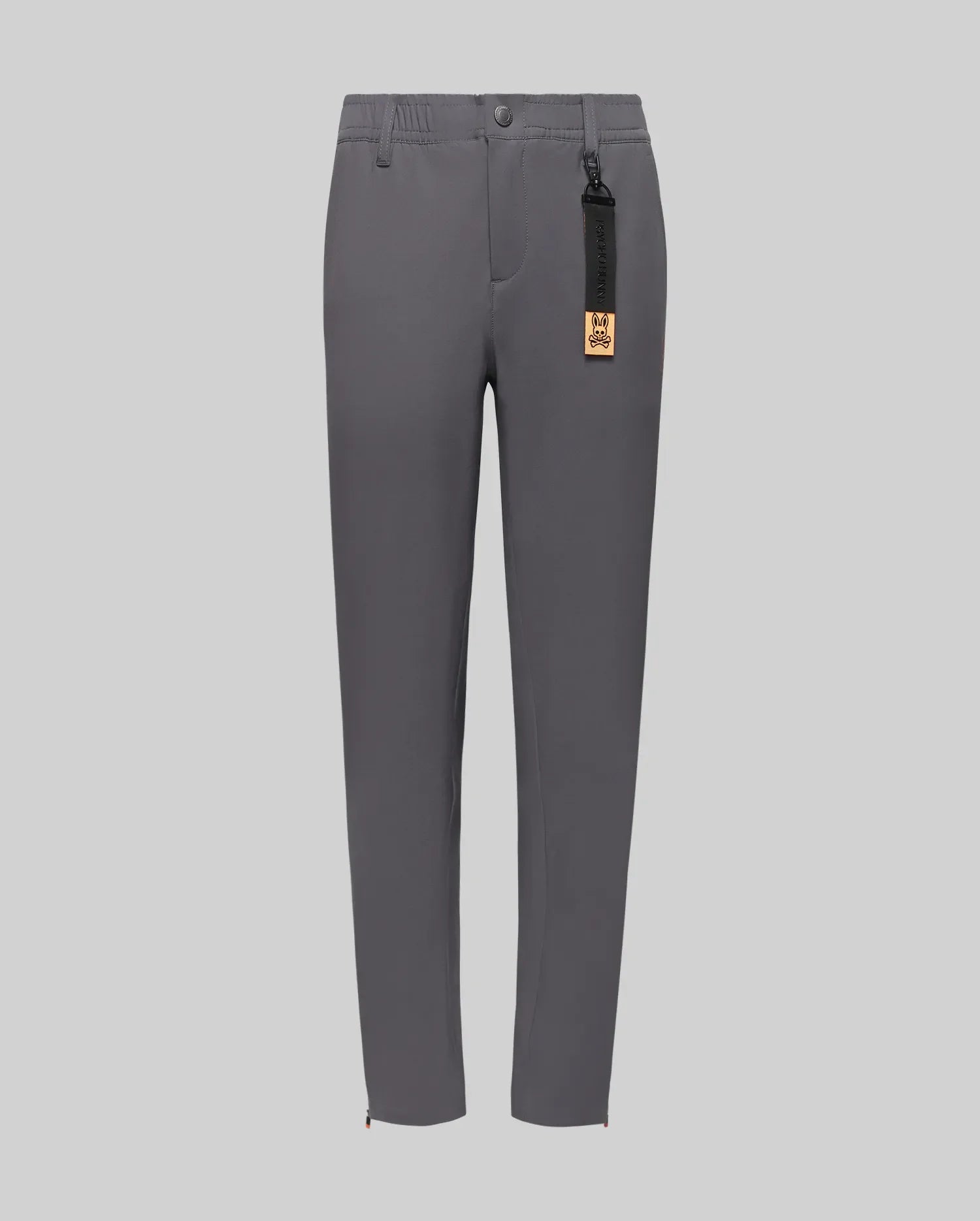The Psycho Bunny KIDS MATHIEU COMMUTER PANT (KB0600002) features a classic fit, straight-leg gray style with front pockets, button and zipper closure, partial elastic waistband, and a black tag with gold label on the belt loop.