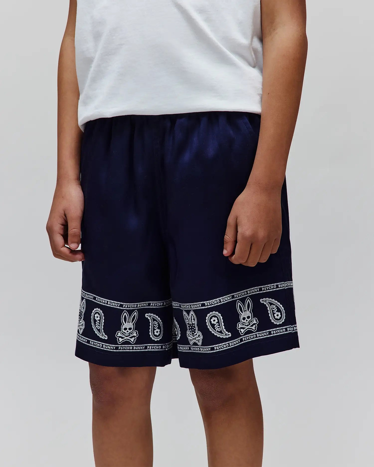 Kids Luke Tencel Short in navy blue with a relaxed fit, featuring a white paisley and Psycho Bunny skull logo pattern band around the hem, with PSYCHO BUNNY text.