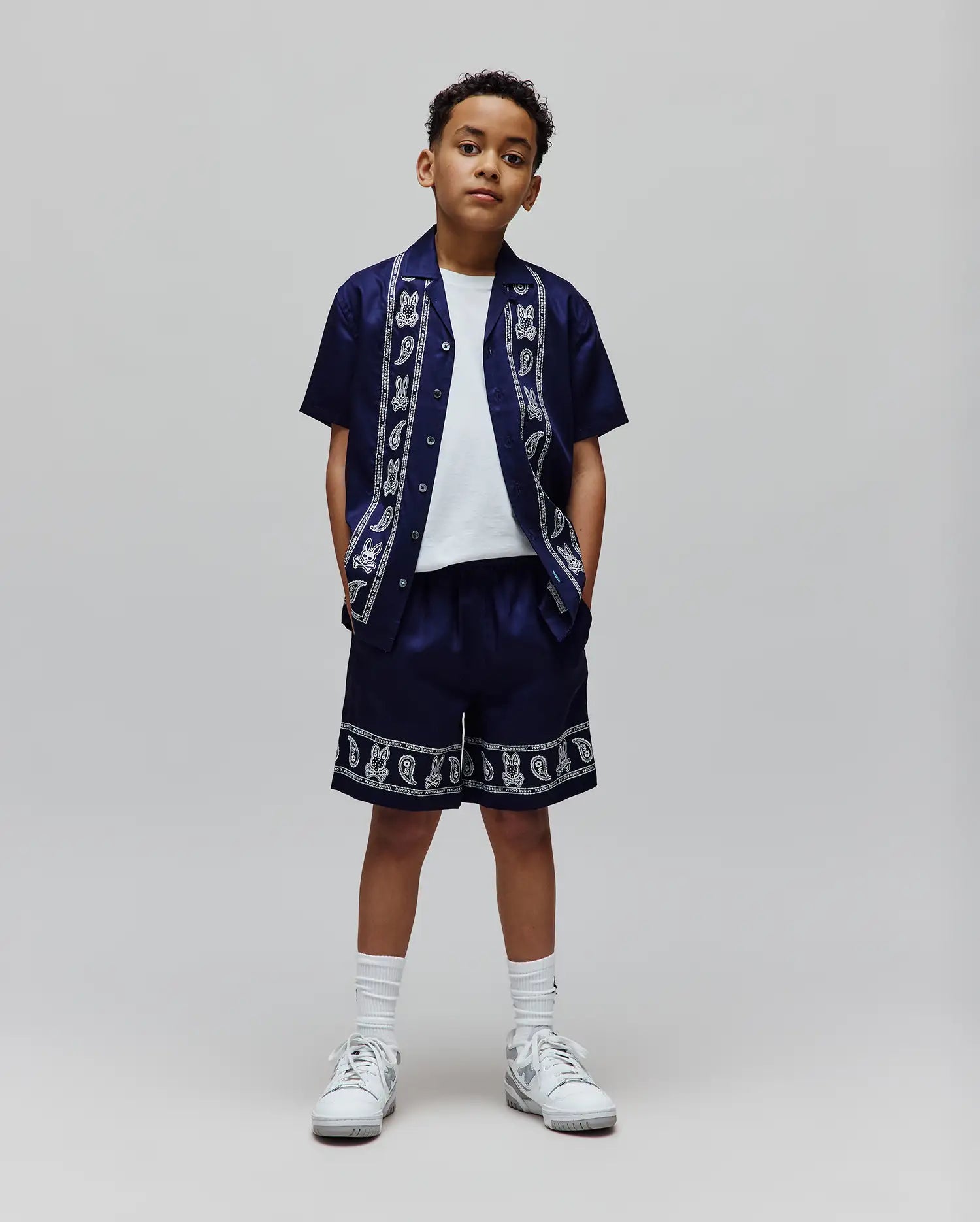 Navy relaxed fit short-sleeve shirt and Kids Luke Tencel Short set, both with a white border pattern of Psycho Bunny skull logos, paisley, and text along the shirt placket and short hem.