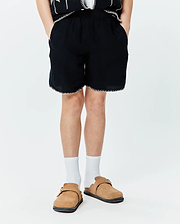 Kids Brad Linen Short, black relaxed fit linen shorts with elastic waistband, white contrast stitching on hem, and a subtle embroidered Psycho Bunny skull logo on the lower left leg.