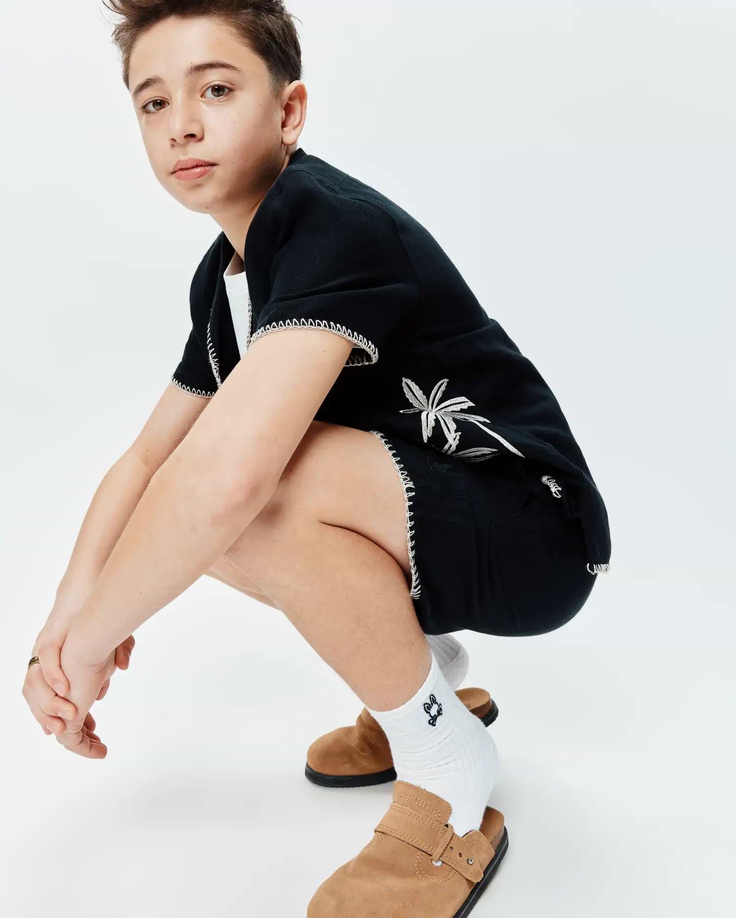 Black Kids Brad Linen Short and matching short-sleeve top with white contrast stitching and embroidered palm tree graphics, paired with white crew socks featuring a small Psycho Bunny skull logo.