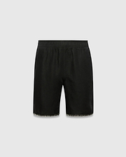 Kids Brad Linen Short, black relaxed fit with linen texture, featuring a subtle tonal embroidered Psycho Bunny skull logo on the lower right leg and white contrast blanket stitching on the hem.