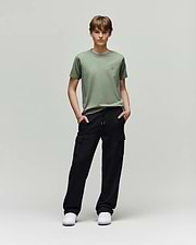 A young person faces forward, wearing a light green t-shirt, white sneakers, and Psycho Bunny KIDS NASH CARGO SWEATPANT - KB0800004 with cargo pockets, hands in pockets, enjoying sweatpant comfort against a plain light gray background.