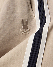 Kids Ty French Terry Sweatpant in beige french terry fabric, featuring a small embroidered Psycho Bunny skull logo and a navy and white side stripe.