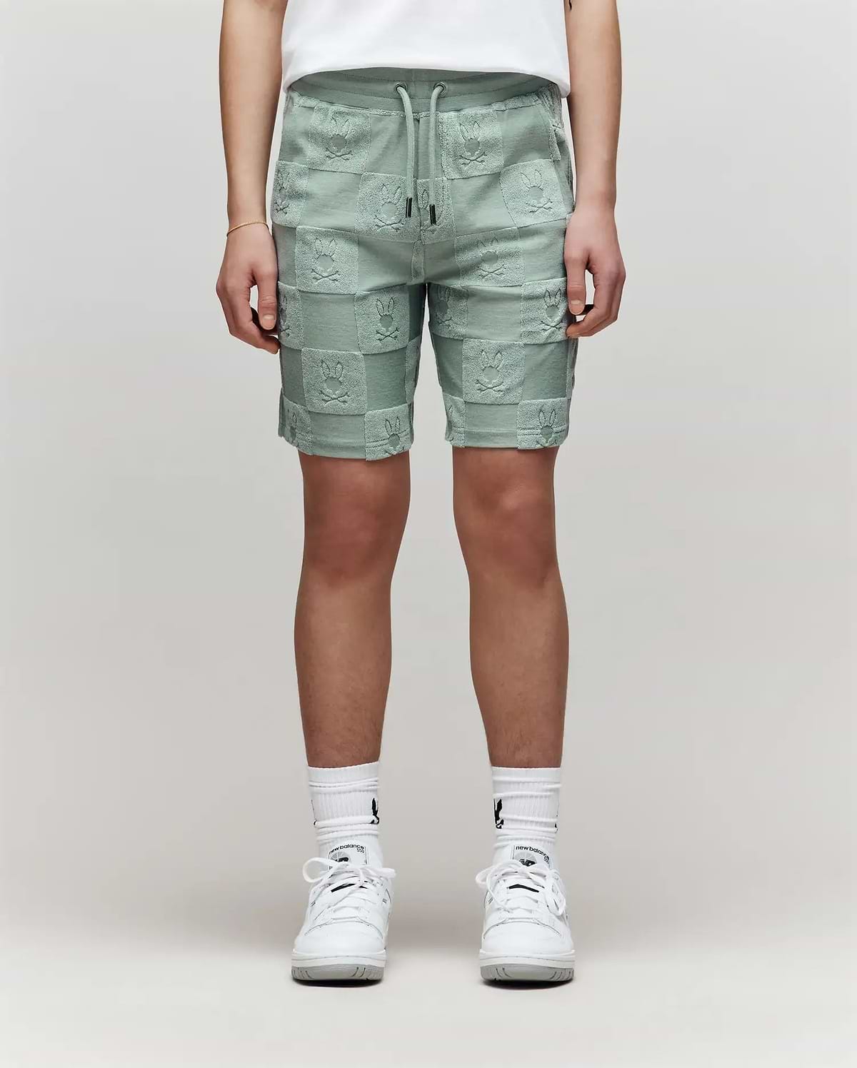 Teen | The lower half of a person is shown wearing Psycho Bunny KIDS KELVIN TOWEL TERRY SWEATSHORT - KB0900002 in mint green, paired with white crew socks and sneakers against a plain background.