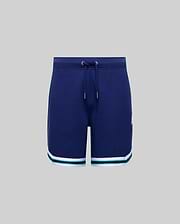 The KIDS BASIL TAPED SHORT (KB0900003) by Psycho Bunny features a navy blue cotton-modal blend with a drawstring waist and white and green striped hems, shown against a plain gray background.