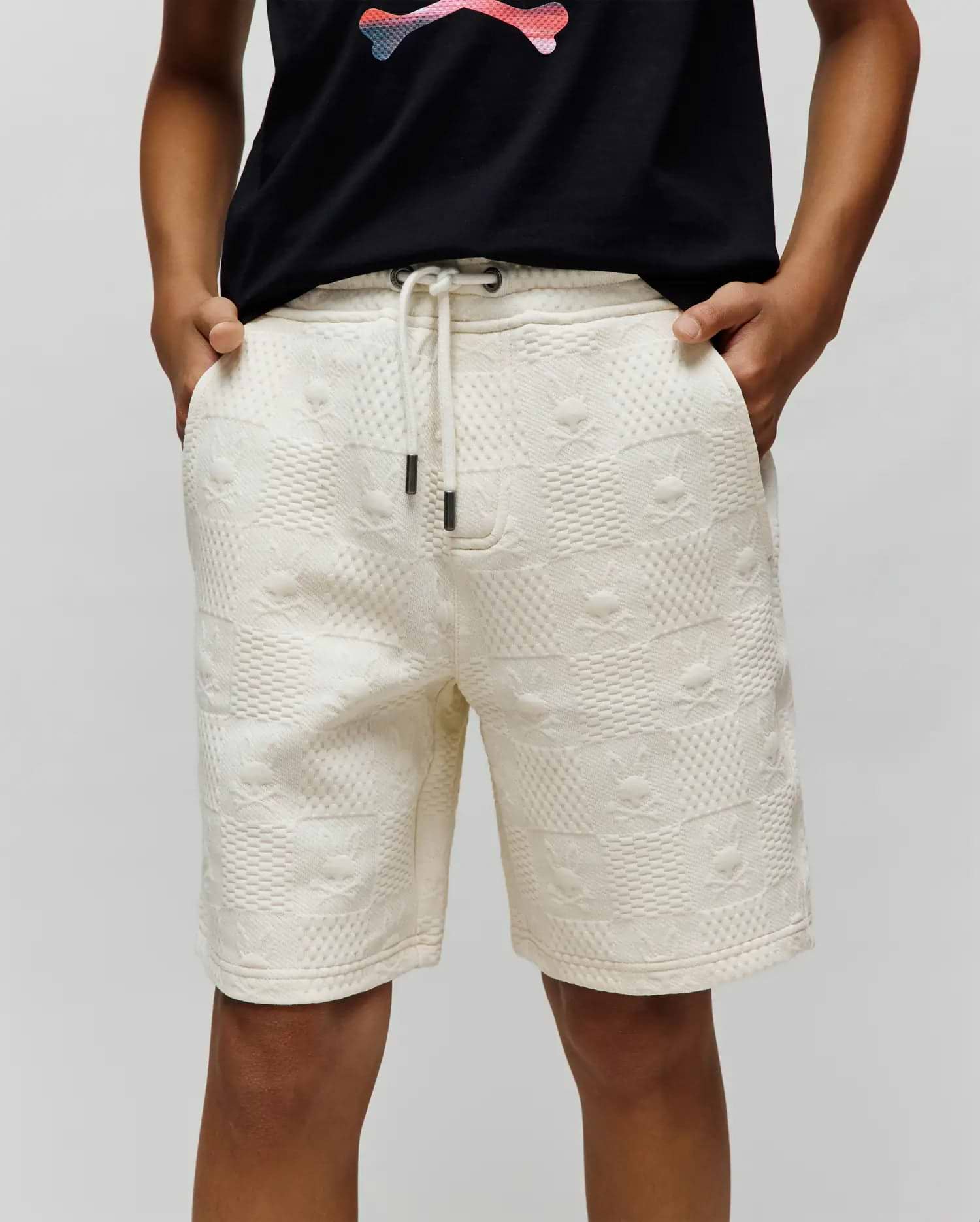 Kids Dustin Sweatshort in cream, featuring a relaxed fit and textured jacquard fabric with an all-over embossed checkerboard pattern of small Psycho Bunny skull logos. Dark drawstring tips.