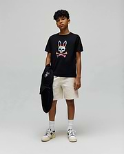 Black jersey t-shirt with a large colorful Psycho Bunny skull graphic, paired with cream Kids Dustin Sweatshort featuring a subtle textured pattern, and a black hoodie with a small embroidered bunny logo.