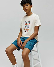 Cream jersey t-shirt with a large multi-color plaid Psycho Bunny logo on the chest, paired with Kids Barry Modal Short in teal, featuring a small embroidered bunny skull logo on the left thigh.