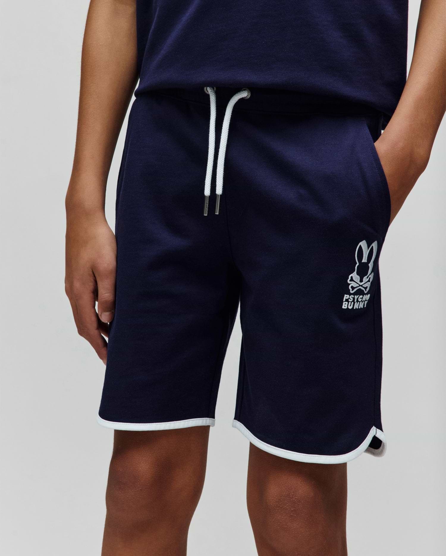 Kids Toby Short, navy relaxed fit jersey shorts featuring white drawstrings, white piping on the rounded hem, and an embroidered white Psycho Bunny skull logo on the left thigh.