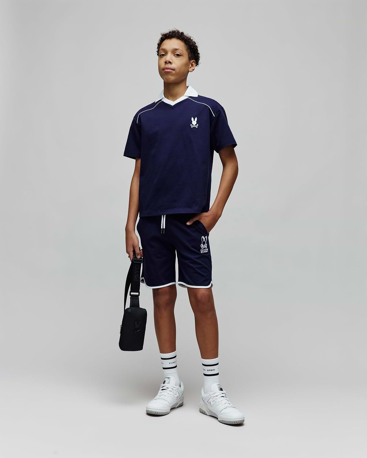 Navy blue jersey t-shirt with white V-neck collar, piping, and embroidered Psycho Bunny logo on chest, paired with Kids Toby Short in navy, featuring white piping and large PSYCHO BUNNY graphic.