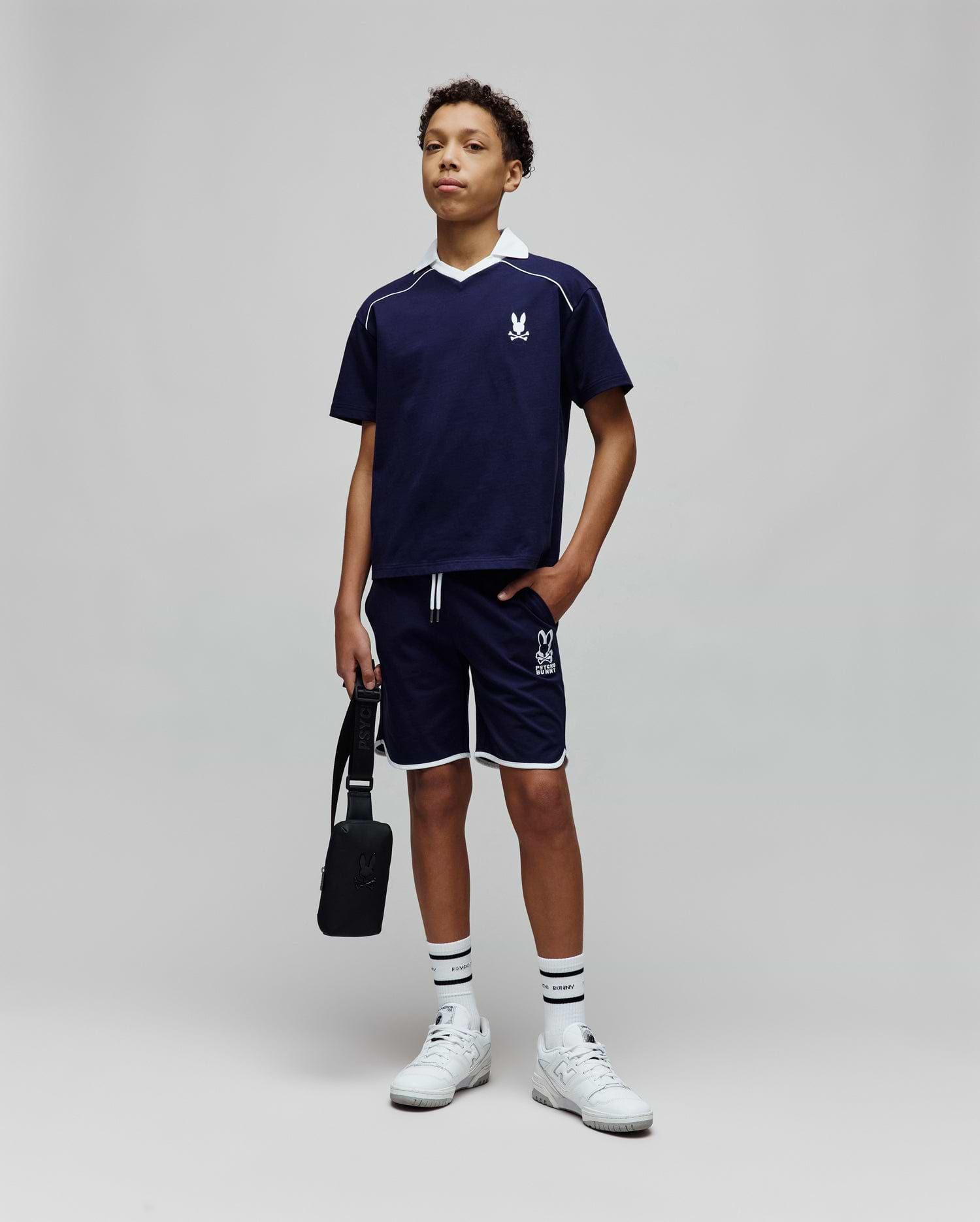 Navy blue jersey t-shirt with white V-neck collar, piping, and embroidered Psycho Bunny logo on chest, paired with Kids Toby Short in navy, featuring white piping and large PSYCHO BUNNY graphic.