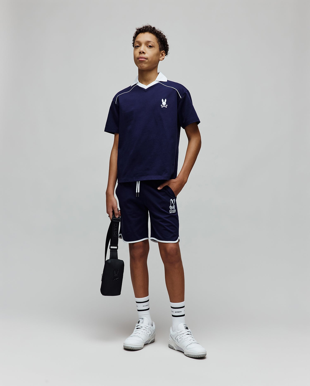 Navy blue jersey t-shirt with white V-neck collar, piping, and embroidered Psycho Bunny logo on chest, paired with Kids Toby Short in navy, featuring white piping and large PSYCHO BUNNY graphic.