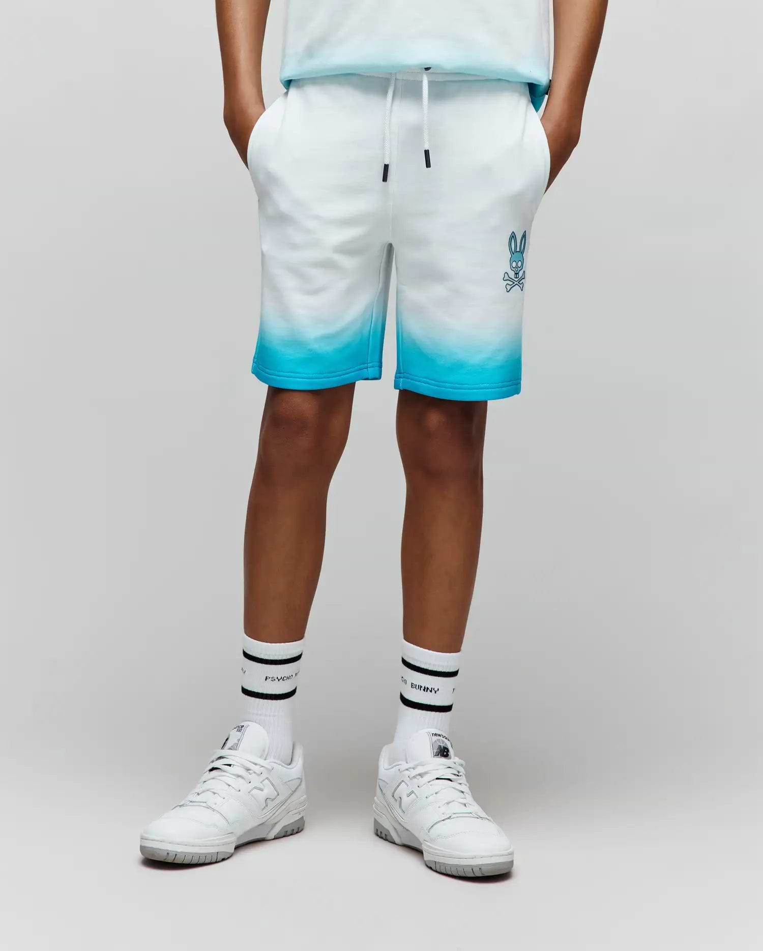 Kids Dax Sweatshort in white french terry, featuring a vibrant blue ombre fade from mid-thigh to hem, with an embroidered blue Psycho Bunny skull logo on the left thigh and a drawstring waist.