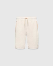 Kids Keith Short, cream textured knit with relaxed fit, featuring a matching drawstring waist, side pockets with cream trim, and a small light blue embroidered Psycho Bunny skull logo on the lower left leg.
