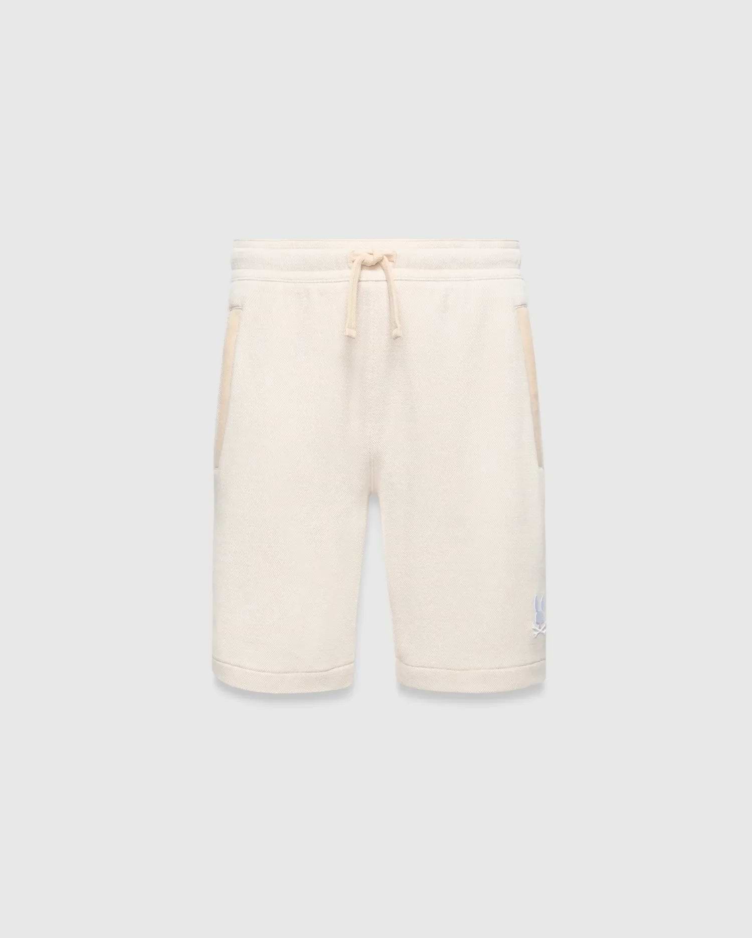 Kids Keith Short, cream textured knit with relaxed fit, featuring a matching drawstring waist, side pockets with cream trim, and a small light blue embroidered Psycho Bunny skull logo on the lower left leg.