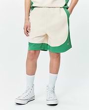 Kids Kelly Short, a relaxed fit cream and green color block short with a curved design, soft jersey fabric, and a small embroidered Psycho Bunny skull logo on the right leg.