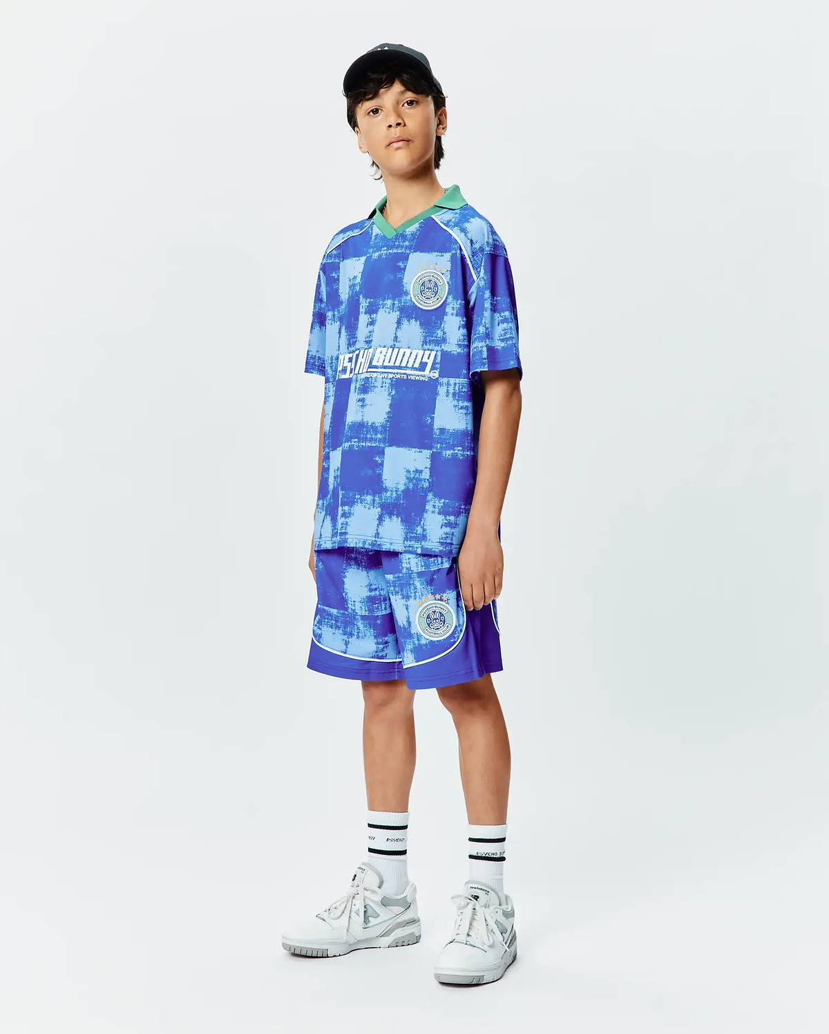 Kids Micah Soccer Short and matching jersey in blue distressed checkerboard pattern with green collar, white trim, and Psycho Bunny crest logos on chest and leg.