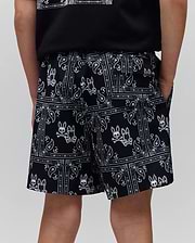 Kids Luke Swim Trunk in black with a white all-over bandana print featuring the iconic Psycho Bunny skull and crossbones logo, a relaxed fit, and smooth fabric.