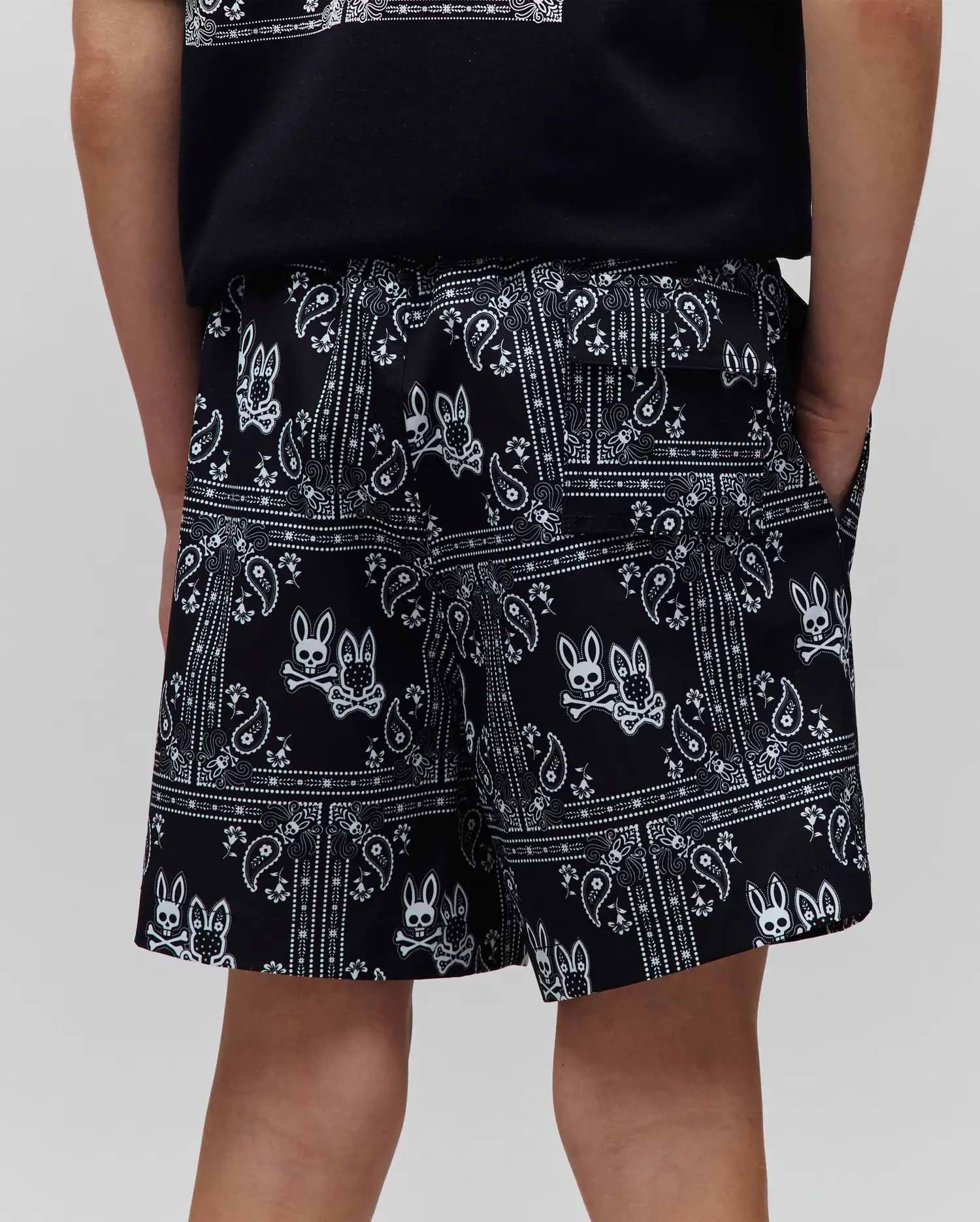 Kids Luke Swim Trunk in black with a white all-over bandana print featuring the iconic Psycho Bunny skull and crossbones logo, a relaxed fit, and smooth fabric.