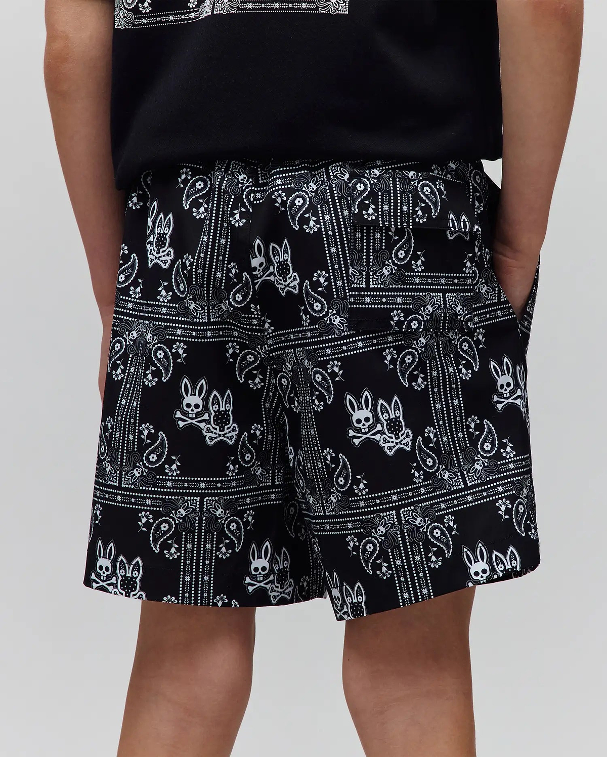 Kids Luke Swim Trunk in black with a white all-over bandana print featuring the iconic Psycho Bunny skull and crossbones logo, a relaxed fit, and smooth fabric.