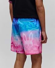 Kids Caspian Swim Trunk in a vibrant blue to pink gradient, featuring an all-over print of large and small Psycho Bunny skull and crossbones logos with a splatter effect.